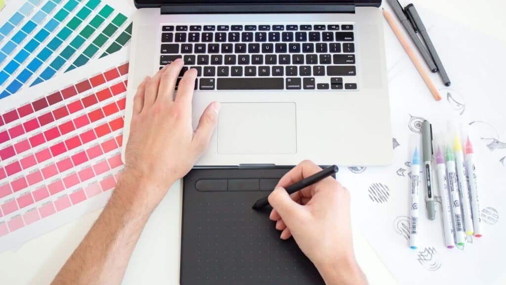 Designer working with color swatches, markers and a drawing tablet, practising the design skills AI can't replace