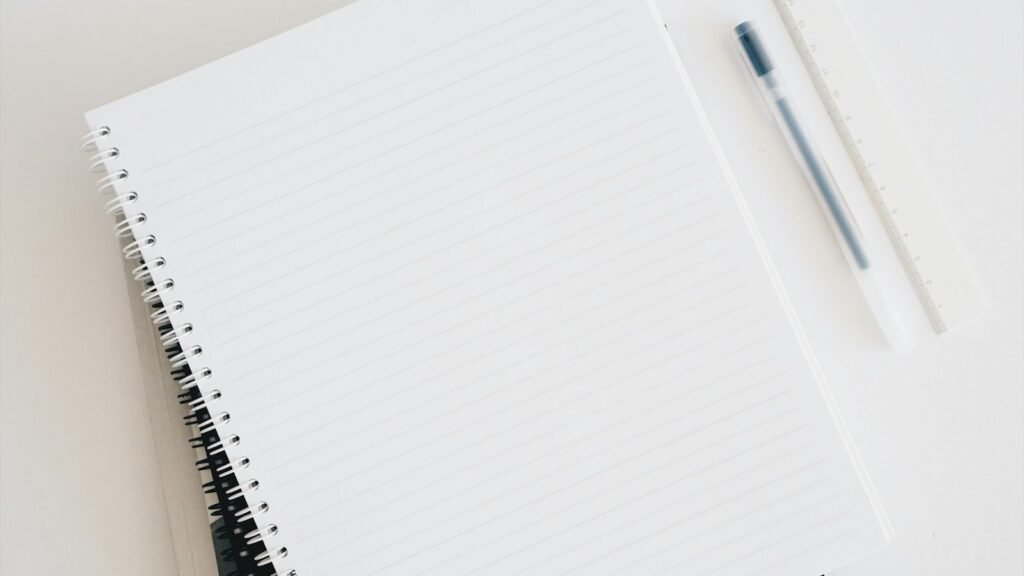 Empty spiral notebook and pen beside a keyboard, for someone learning to become a UX designer without a degree